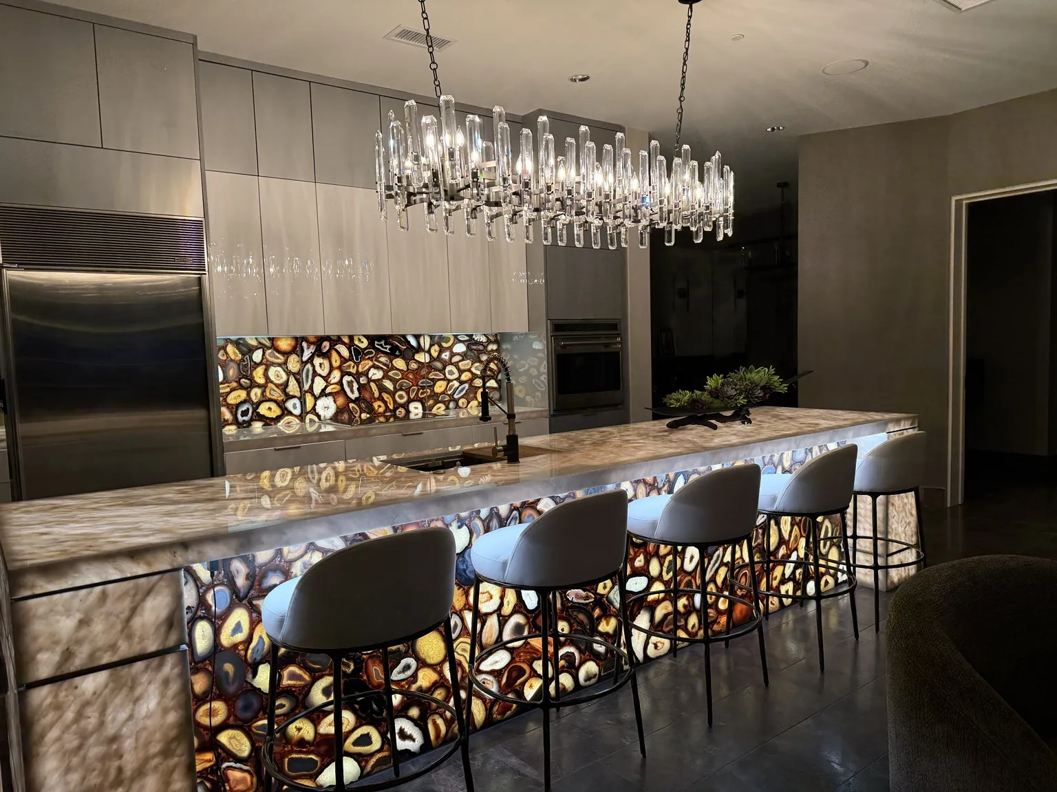 Backlit agate kitchen island with crystal pendant lighting in a finished Bad BHouse project
